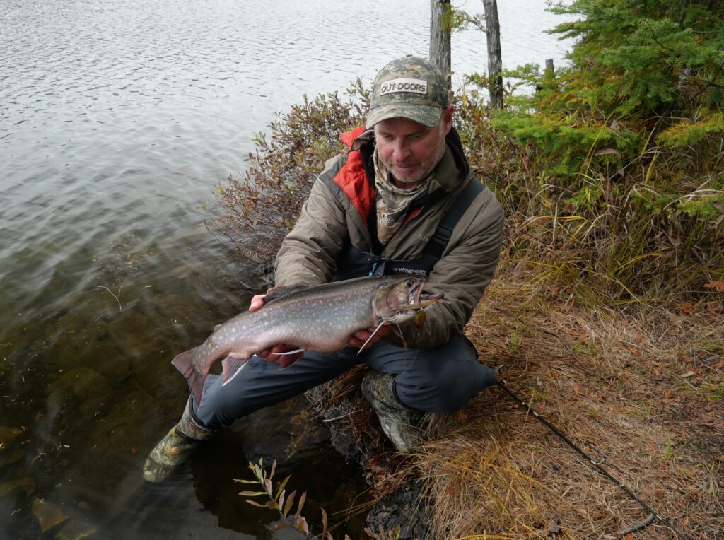 An angler proudly holds a freshly caught brook trout on the banks of a creek, its vibrant colors glistening against the serene waters—making the most of put-and-take fishing opportunities.