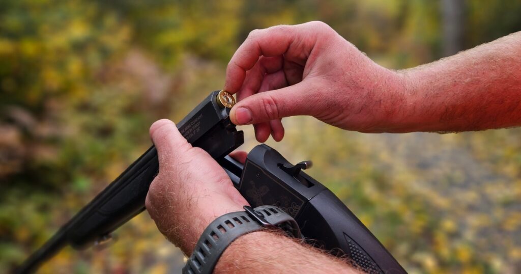 A break-action 28-gauge shotgun being loaded with a shell, held securely in a hunter's hand.