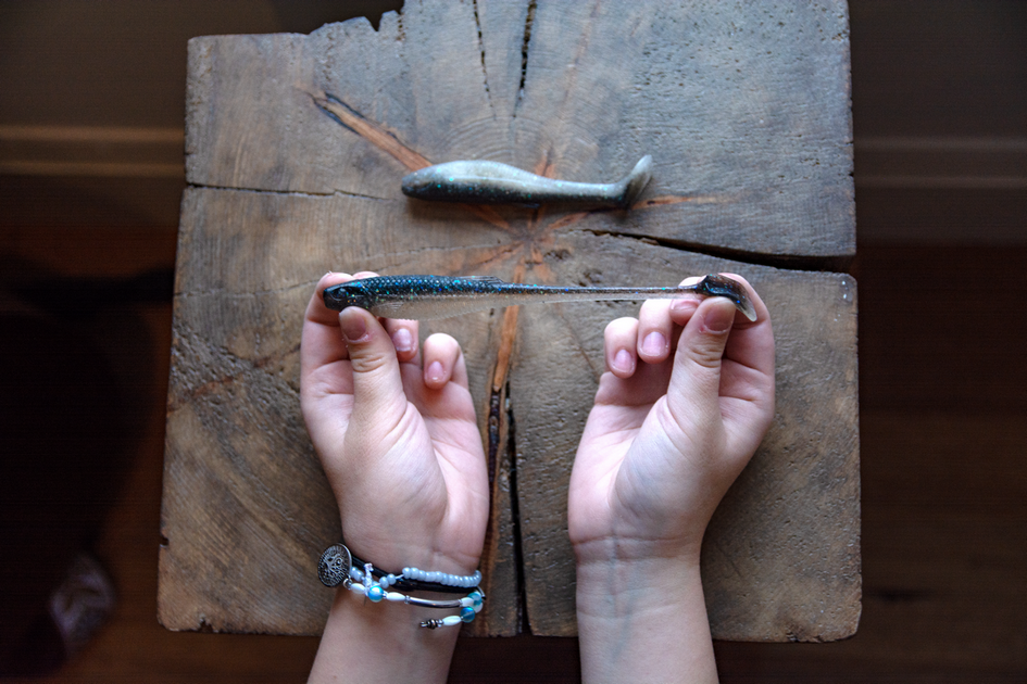 Plastic fishing bait in two hands, resting on a wooden block