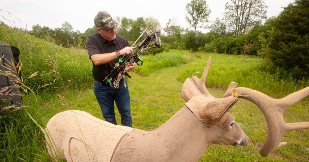 An archer removes an arrow from his quiver with a 3D archery deer target in view.